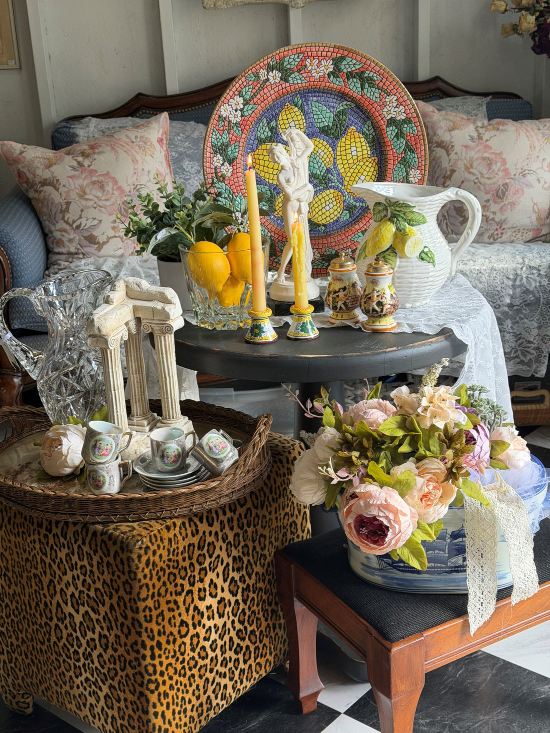 A beautifully curated vintage vignette featuring mosaic art, crystal pitchers, antique ceramics, candles, and fresh florals