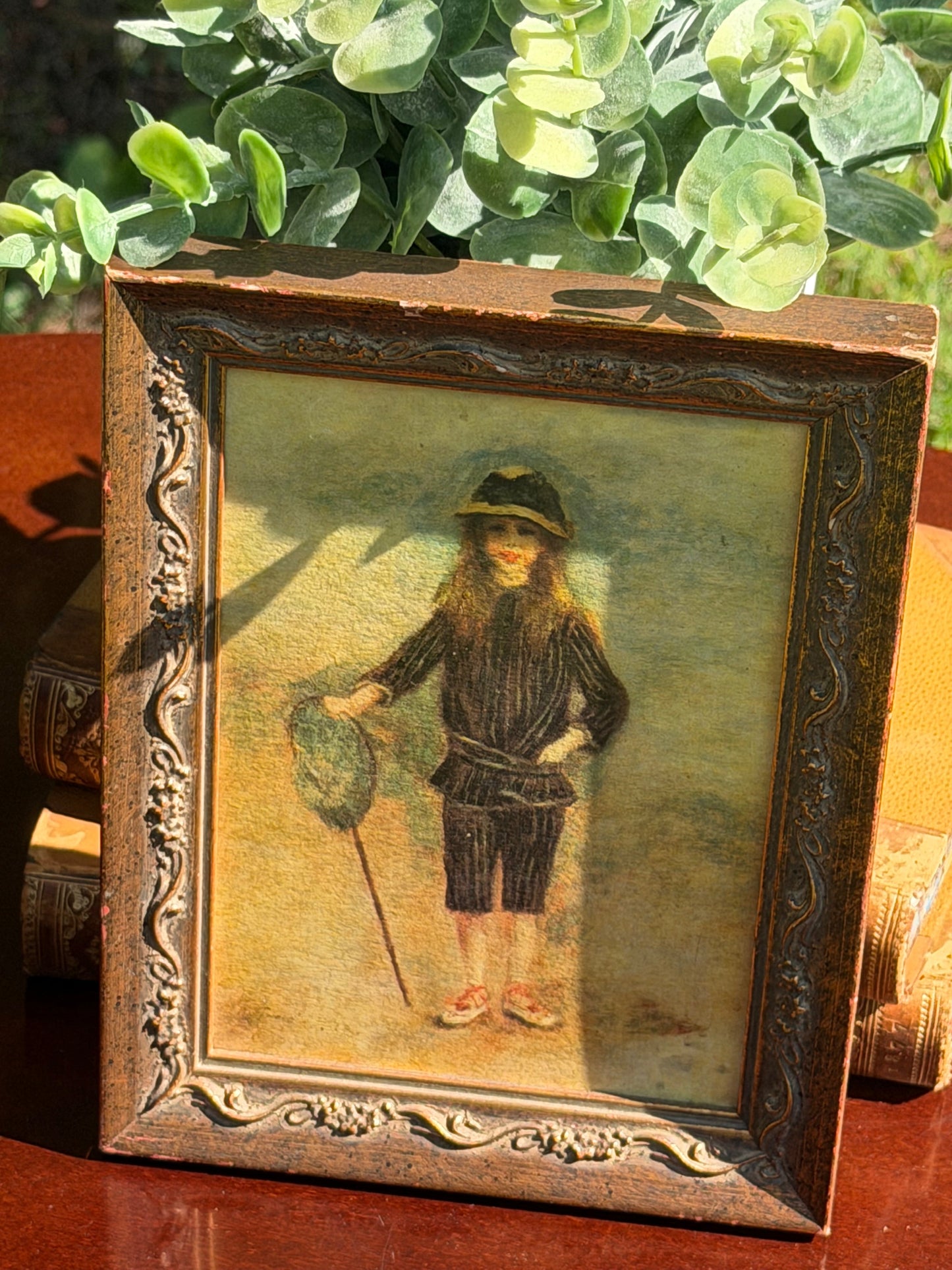 Front view of Renoir Fisher Boy framed print leaning against vintage books outdoors